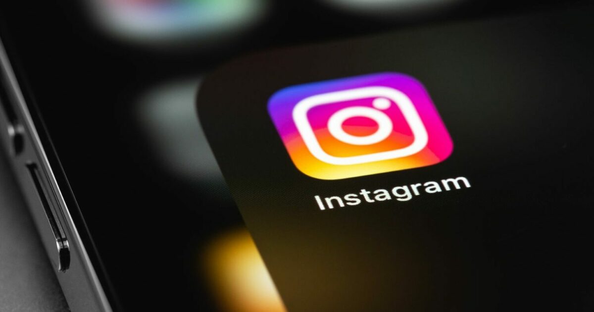 Ícone do aplicativo Instagram exibido na tela de um smartphone, com cores vibrantes em tons de roxo, rosa e laranja, contrastando com o fundo escuro do dispositivo. A imagem representa o acesso ao Instagram e o uso de redes sociais em dispositivos móveis