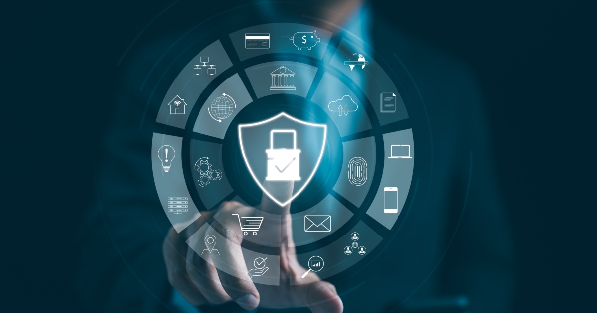 Imagem de uma interface digital com um escudo no centro, simbolizando segurança cibernética. Ao redor, ícones representando tecnologias, serviços e dados, como nuvem, e-commerce, biometria e dispositivos móveis. Uma mão humana toca a tela, destacando o conceito de interação e proteção digital (riscos cibernéticos, cibersegurança, Syxsense, Red Hat, ataques, brasil, negócios, software, ataque)