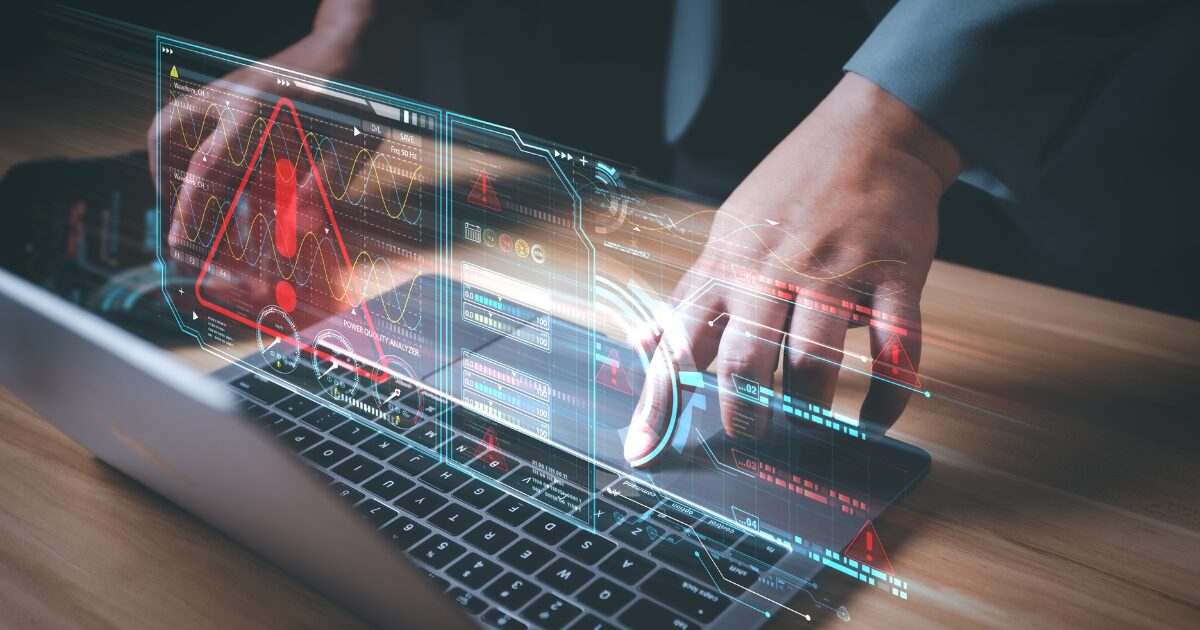 A imagem apresenta um laptop com a tela exibindo gráficos holográficos avançados e elementos digitais flutuantes. Um grande ícone de alerta vermelho com um ponto de exclamação ocupa o centro, indicando um possível erro ou situação crítica. Ao fundo, há gráficos de ondas, indicadores de desempenho e barras de progresso coloridas. As mãos de uma pessoa, vestindo roupa formal, brasil,interagem com o teclado, sugerindo um ambiente de análise tecnológica ou de gestão de sistemas críticos. A composição transmite uma sensação de alta tecnologia e monitorização em tempo real.