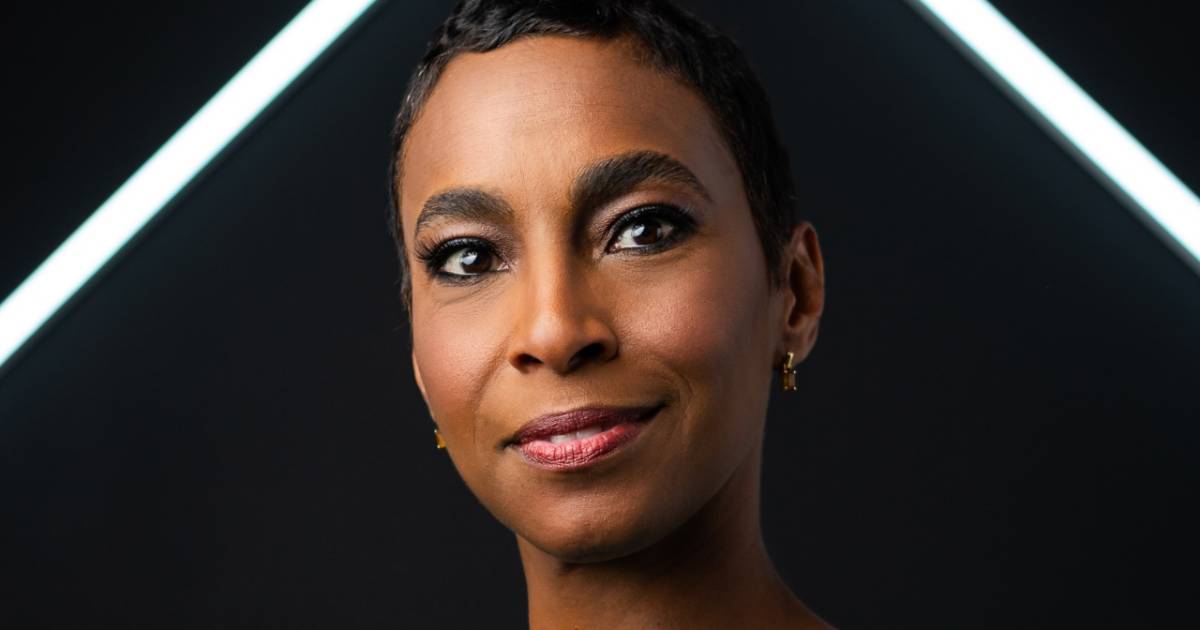 Dilma Sousa Campos, CEO da Nova Praia e CSO da B&Partners.co, em close-up, com expressão confiante e leve sorriso, usando brincos pequenos dourados. O fundo é escuro com linhas diagonais de luz branca, criando um visual moderno e sofisticado.