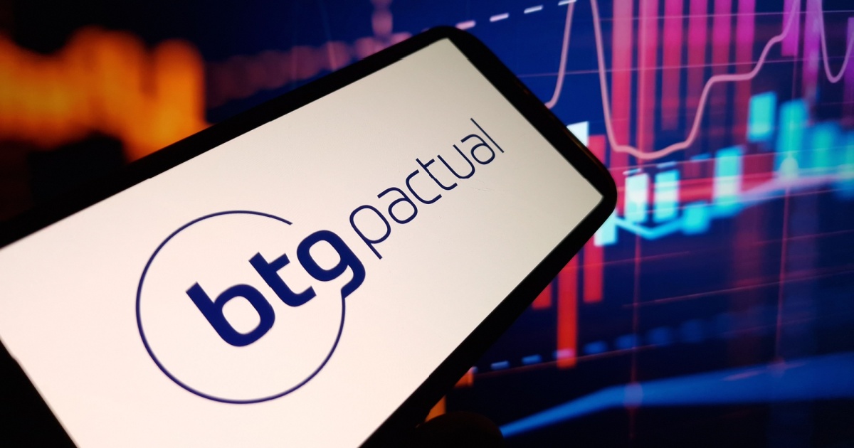 A imagem mostra um smartphone exibindo o logotipo do BTG Pactual, um banco de investimentos brasileiro. O fundo contém gráficos financeiros com linhas e barras coloridas, sugerindo um ambiente de mercado financeiro ou bolsa de valores (assistente, ia, inteligência artificial)