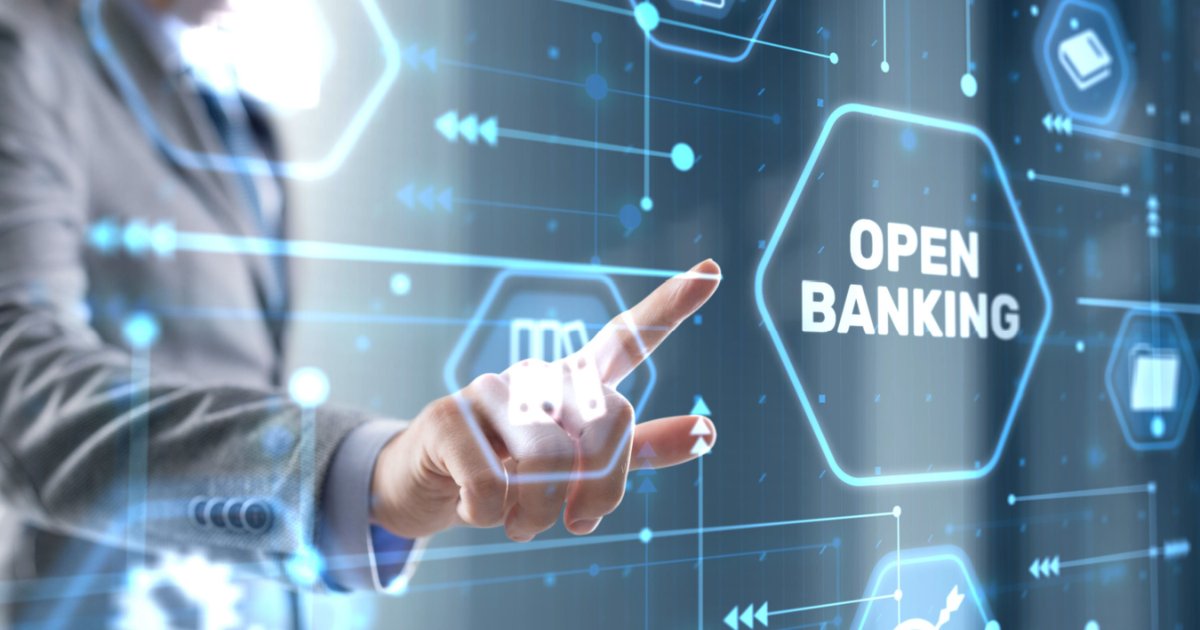 Imagem conceitual sobre Open Banking. Uma mão apontando para um painel digital com o texto 'OPEN BANKING' destacado em um hexágono luminoso. O fundo apresenta ícones tecnológicos e conexões digitais em tons de azul, representando a integração e o compartilhamento de dados financeiros de forma segura e transparente, consentimentos (fintech)