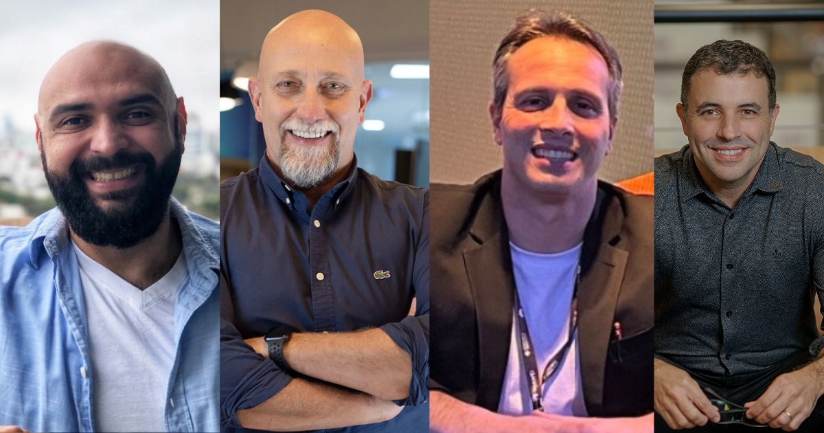 Quatro homens estão lado a lado, sorridentes, em ambientes distintos. Da esquerda para a direita: o primeiro tem barba cheia, cabeça rapada, veste uma t-shirt branca com camisa azul clara; o segundo é careca, com cavanhaque grisalho, veste camisa azul escura com as mangas arregaçadas; o terceiro tem cabelo curto grisalho, usa blazer preto com t-shirt branca; o quarto tem cabelo curto e escuro, usa camisa cinzenta escura e segura uns óculos. Todos transmitem uma imagem descontraída e profissional.