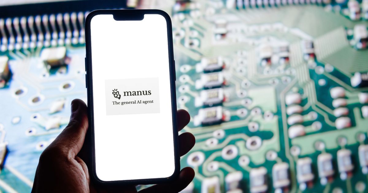 Mão segurando um smartphone com o ecrã a exibir o logótipo da "Manus – The general AI agent", sobre um fundo branco. Ao fundo, desfocado, vê-se um circuito eletrónico verde, repleto de componentes, simbolizando tecnologia e agente de inteligência artificial (agente)