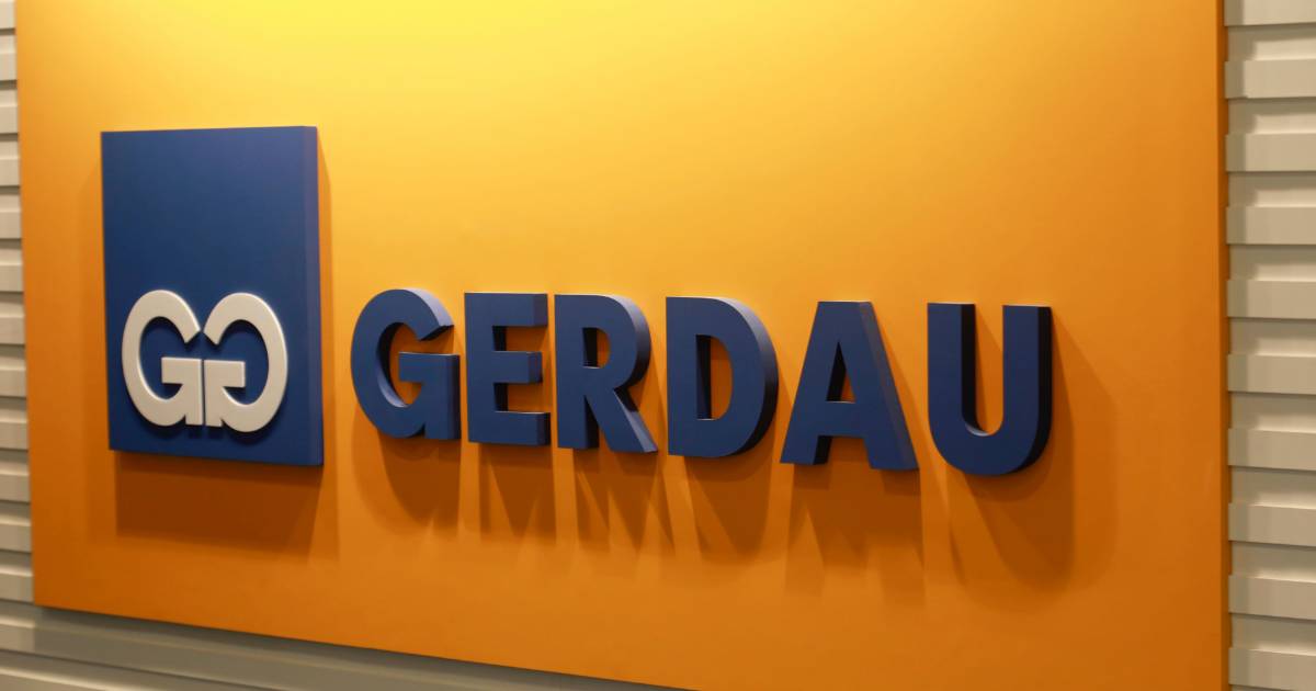 Painel interno com o logotipo da empresa Gerdau em letras azuis em relevo sobre um fundo amarelo. À esquerda, o símbolo da marca aparece em azul com o monograma "GG" em branco. O painel está instalado sobre uma parede com acabamento metálico.